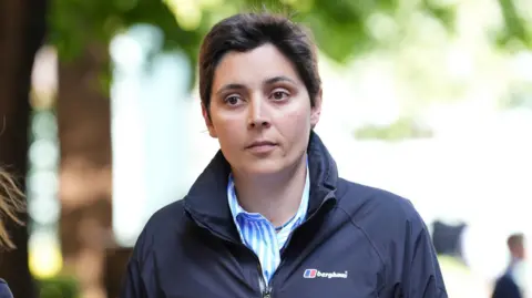 PA Media A woman with short hair wearing a dark, plain Berghaus jacket and a blue and white striped shirt with a collar.