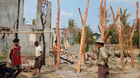 This photo taken on May 21, 2024 shows people rebuilding temporary homes near a destroyed building following fighting between Myanmar's military and the Arakan Army (AA) ethnic minority armed group in a village in Minbya Township in western Rakhine State