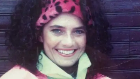 Jordan and Cian Adams Geraldine Adams smiles. She is wearing a neon pink leopard print headband and a bright luminous jacket.