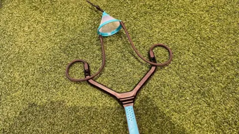A brown catapult with blue handle on grass