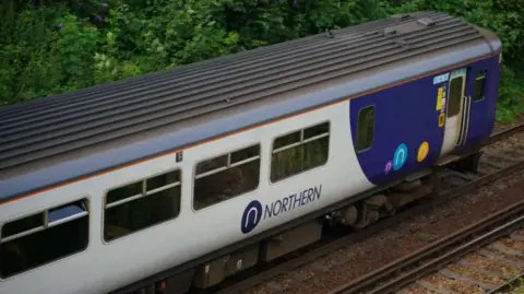 Northern train in its customary white and dark blue colours travelling on a railway track with shrubs in the background