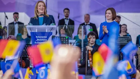 ELENA COVALENCO/AFP European Parliament President Roberta Metsola (C) address to the people as Moldova's President Maia Sandu (C,R) listens on, during a pro-EU rally in Chisinau on May 21, 2023. Met