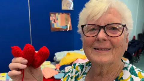 Marilyn Wyatt holding up a pair of knitted hearts