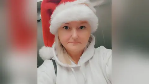 Family photograph Amanda Thompson with blond hair wearing a red and white Santa hat and cream hoodie. 