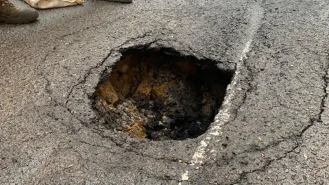 Mick Lunney/BBC A hole in concrete. Some chunks of concrete have fallen into the floor. It is unclear how deep it is due to the angle of the picture. There are lines surrounding the hole where the ground has cracked further.