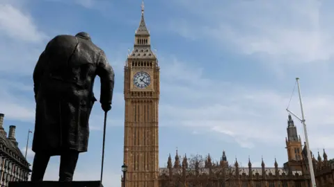 The back of the bronze statue of Churchill leaning on a walking stick, with Big Ben and parliament in the background