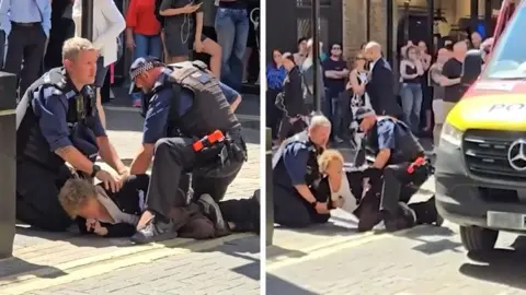 Officers make an arrest in a crowded street with a woman on the ground pinned by two officers.