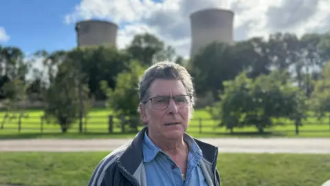 Local resident Jan Folega, wearing a blue shirt and glasses, standing outside with the cooling towers of Cottam in the background