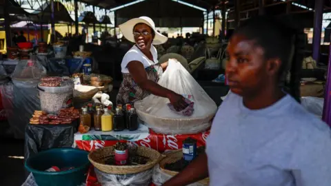 AFP A woman in a market stall wearing a wide-brimmed hat cleans a clean plastic bag that protects a basket of sugar. 