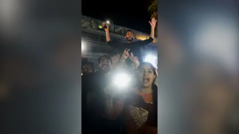 Group of people holding phones with flashlights on and celebrating