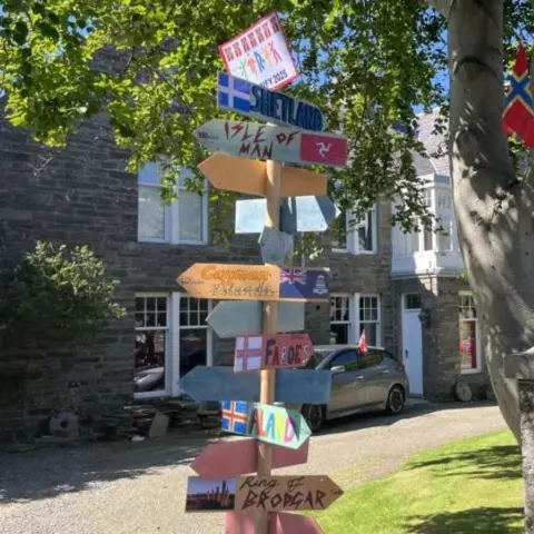 A sign with several signs pointing in different directions with islands painted on the front.