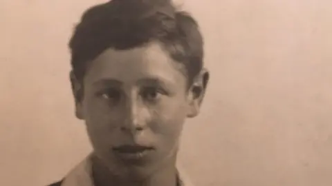 Adrian Goldberg An old sepia photo shows a teenage boy wearing a dark jumper and a white shirt.