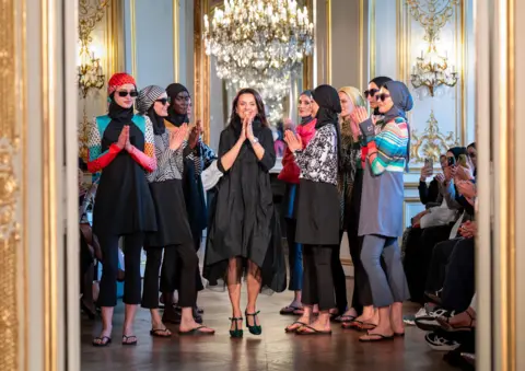 ThinkFashion Several models wearing colourful burkinis - full-length swimsuits coveringe ecerything except the face, hands and feet, on the runway