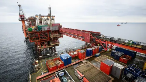 A drilling platform for oil in the North Sea The view is diagonal. A boat can be seen in the distance behind it.
