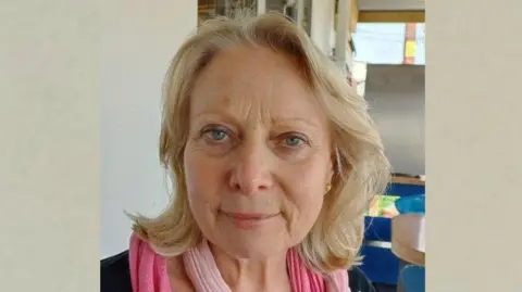 Devon and Cornwall Police A head-and-shoulders image of Judith Law. She is wearing a pink scarf and a black top. Ms Law has blonde, shoulder-length hair and blue eyes and she is smiling directly at the camera.