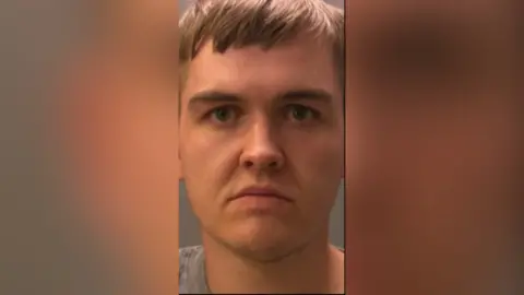 A mugshot of Callum Johnstone. He has dark blond hair with a fringe and wears a severe expression. 