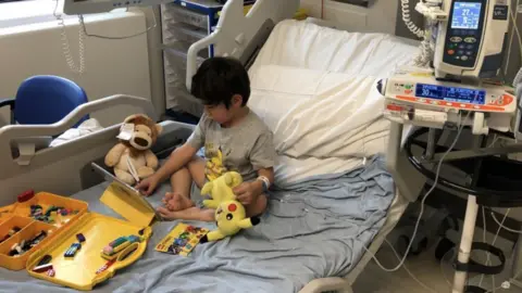 GOSH Joshua sitting on a hospital bed with teddy bears, toys and an iPad.