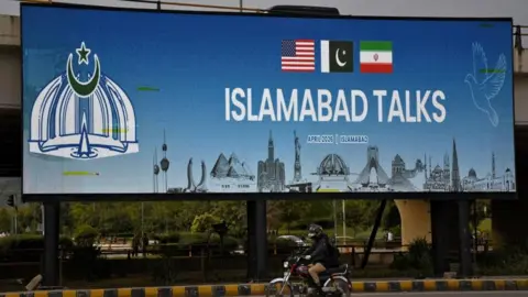 Reuters A motorcyclist rides past a digital billboard which reads 'Islamabad talks' and features a US, a Pakistani and an Iranian flag