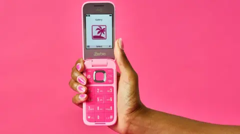 Getty Images A hand holding the phone. It is a bright pink early 00s style flip phone, with big numbers and a small screen. The person has pink nail polish.