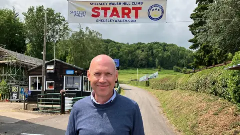 Toby Moody standing at the start of the track. There is a country lane behind him with verges and hedges and a start sign above him. The Worcestershire countryside is behind him.