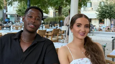 Amy Worrell Tommy and Amy sit in a town square with chairs and tables around them