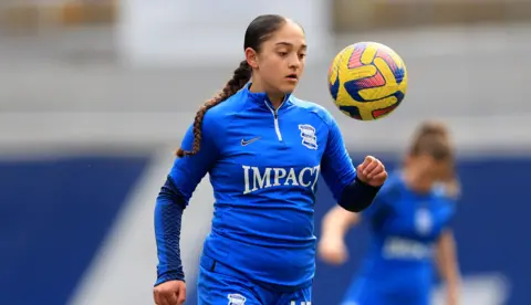 As imagens Getty são Laila, que é azul em seu kit de futebol de Birmingham City. Ele olha para a bola amarela que é a altura da cabeça. No fundo, você verá seus colegas jogadores de futebol.