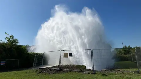 A burst water pipe on a field sends huge burst of water into the air 