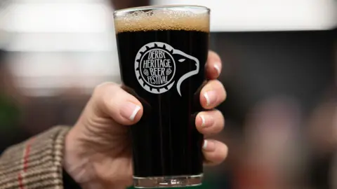 A glass of ale inside a glass reading "Derby Heritage Beer Festival"