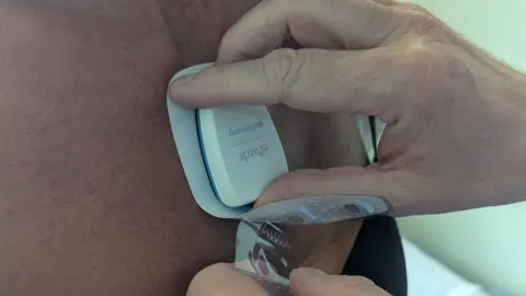 A hand pressing a small white device to a patch of skin