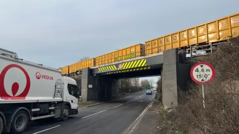 A lorry approaches a bridge as a freight train crosses above