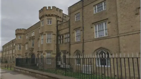 A stone built building has two large turrets, black railings and many large windows