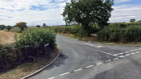 Google Junction of country road with hedges runing alongside it