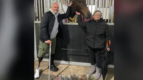 Wayne Hatton and his mother petting a horse at a stable