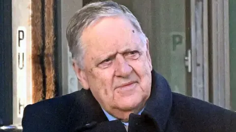 Man with grey hair and black coat.