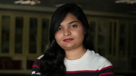 Anahita Sachdev/BBC Zyma Islam, a reporter of the Daily Star newspaper, sitting in the office library in Dhaka and talking to BBC