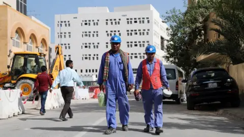 AFP Migrant workers walk next to a construction site in Doha, Qatar (6 December 2016)