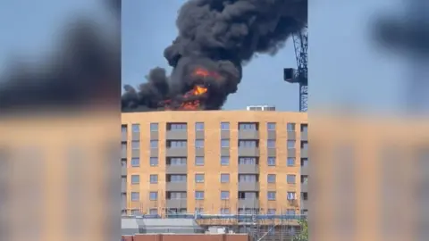 Andrew Mayar Flames are seen on top of a building in Staines