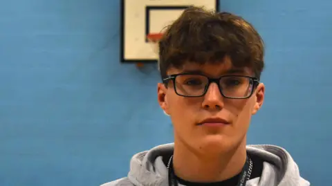 Suffolk New College A head and shoulders image of Henry. He is wearing glasses and a grey hooded top and looking directly into the camera.