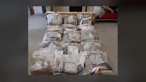 NCA A grainy image of several large clear evidence bags full of cannabis. The bags are lying on a concrete floor.