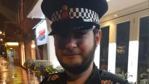 Facebook A close-up image of William Towner in uniform, wearing a peaked cap, standing in a lit street at night with buildings behind.
