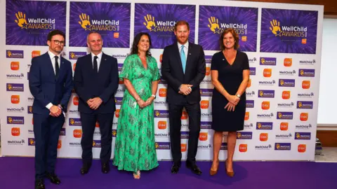 Reuters Prince Harry poses for a representation   with General Manager astatine  Royal Lancaster Hotel Sally Beck, Wellchild CEO Matt James, Wellchild Chair of Trustees Craig Hatch, GSK SVP Global Communications and CEO Office Sally Jackson