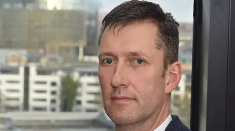 An Garda Síochána A head shot of Justin Kelly. He has short brown hair and is looking at the camera.