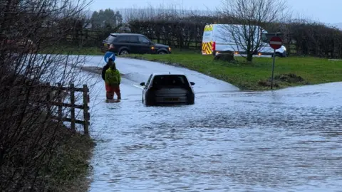 Underpass flooded at Fenny Bridges turn off from A30. There is a car at the centre.