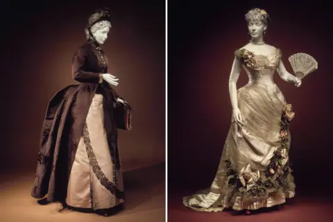 Metropolitan Museum of Art Two images of Victorian dresses on mannequins. The first is a brown and cream afternoon dress with matching hat and bag. The second is in a silver-cream evening dress with intricate ruffles and floral details, with matching fan.