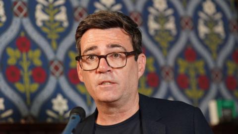 Andy Burnham wearing glasses speaking into a microphone