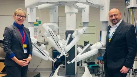 St George's, Epsom and St Helier University Hospitals and Health Group The image shows a man and woman standing beside a white surgical machine with four arms.