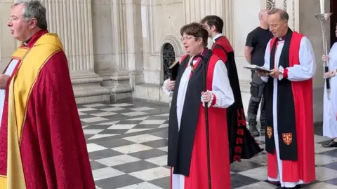 A line of church men and women in formal robes with some holding staffs.