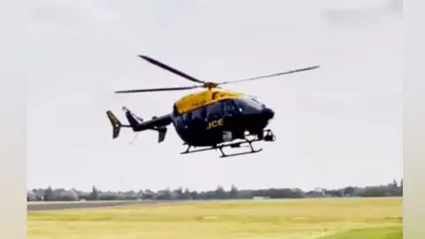 Police helicopter takin off from a field. The lower half is black and the upper half bright yellow, with POLICE in yellow on the lower half.