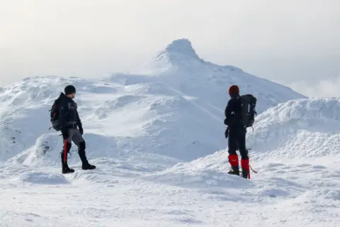 Gareth Overton Two mountaineers with rucksacks and winter gear are looking towards a snowy peak