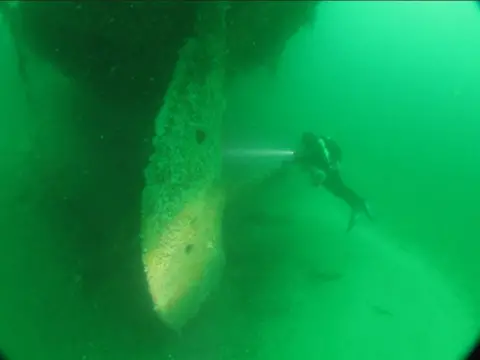 LEIGH MORRIS A man diving on the wreck of the Liverpool. The water is lot green and the ship's rudder can be seen in the fore of the scene.